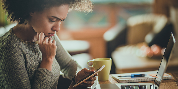 Worried woman looking at cell phone in front of laptop