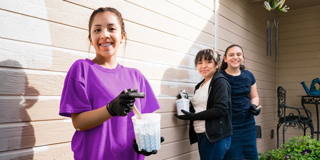 Three girls smiling as they paint the side of a house