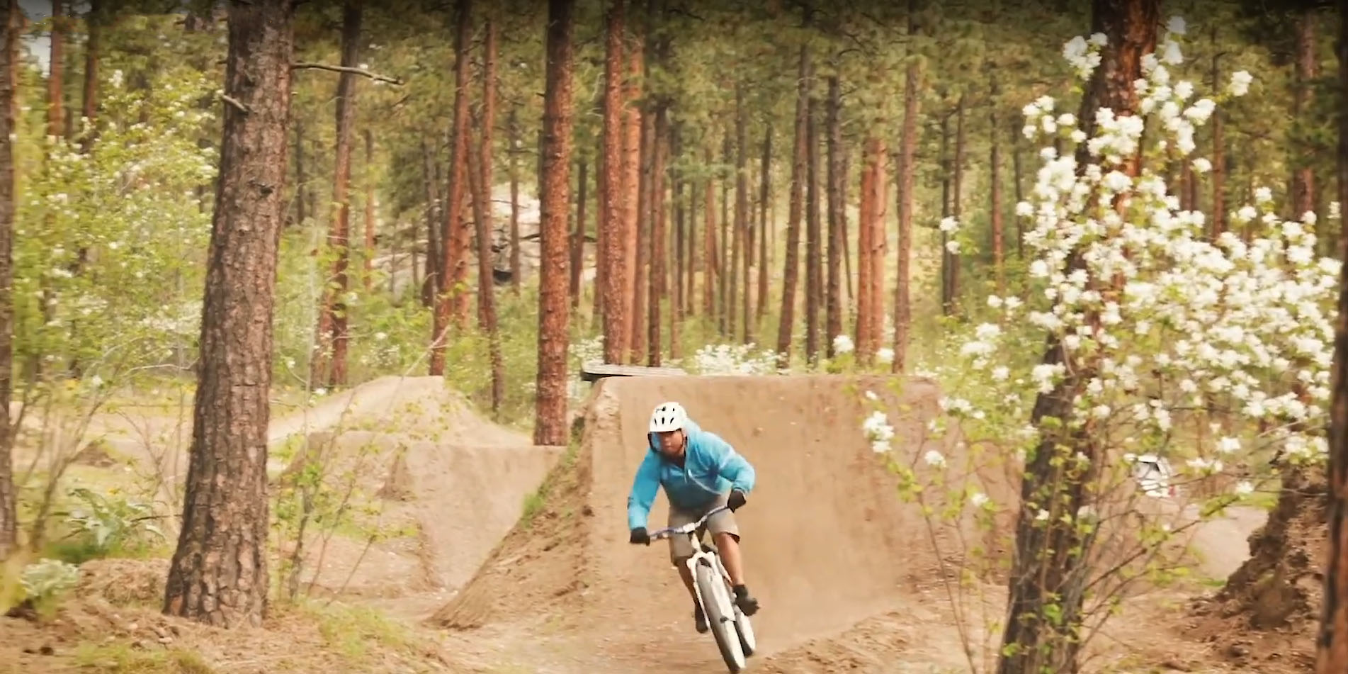 Man biking outside on a dirt track with jumps
