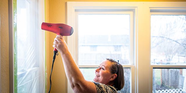 Woman using hairdryer to apply plastic to windows for energy efficiency