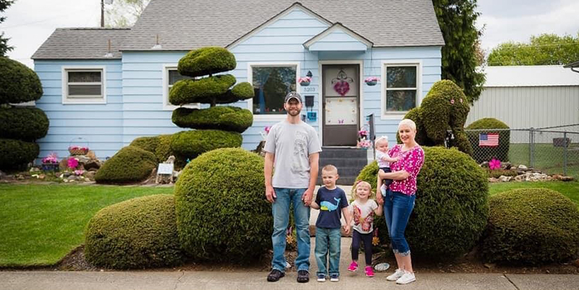 Five person family standing in front of their home - father, mother, little boy, and two little girls