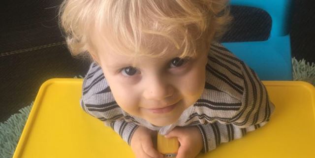 Little boy leaning forward on yellow table, smiling