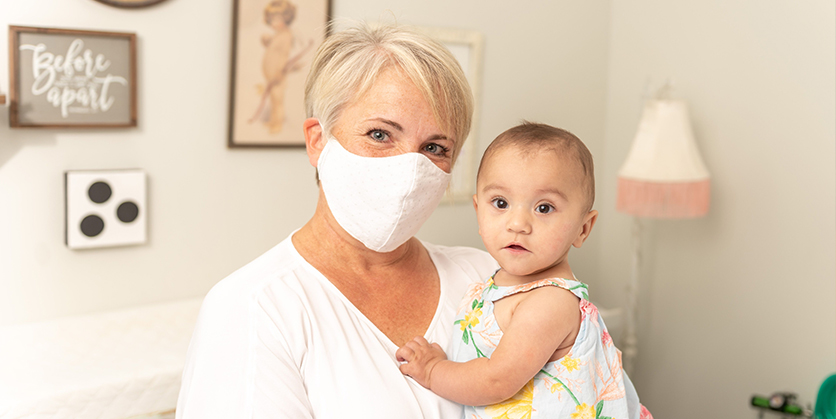 Woman wears a mask and holds a baby in her arms