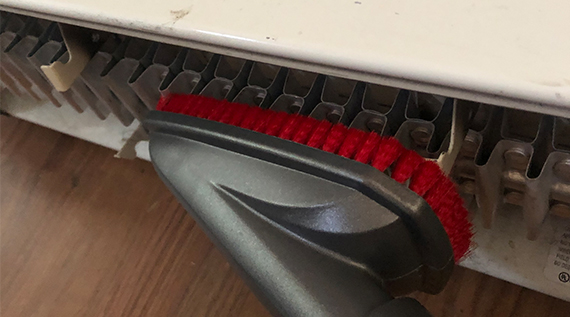 Vacuum with brush attachment cleaning baseboard heater