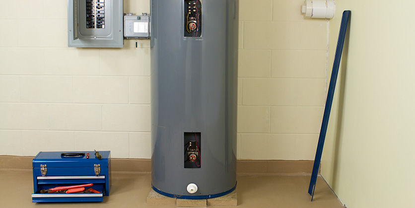 Water Heater with the panel removed to adjust the thermostat. Toolbox sitting on the ground next to it.