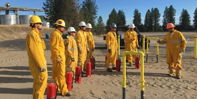 Apprentices lined up listening to an instructor with fire extinguishers sitting at their feet