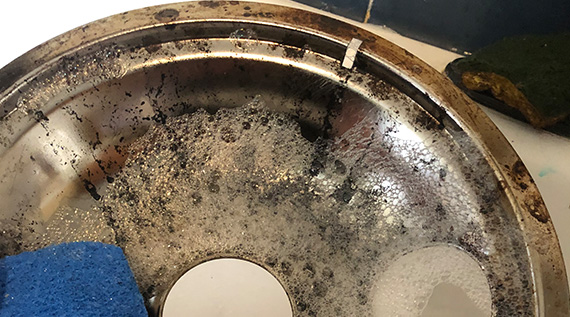 Dirty oven burner being cleaned in soapy water
