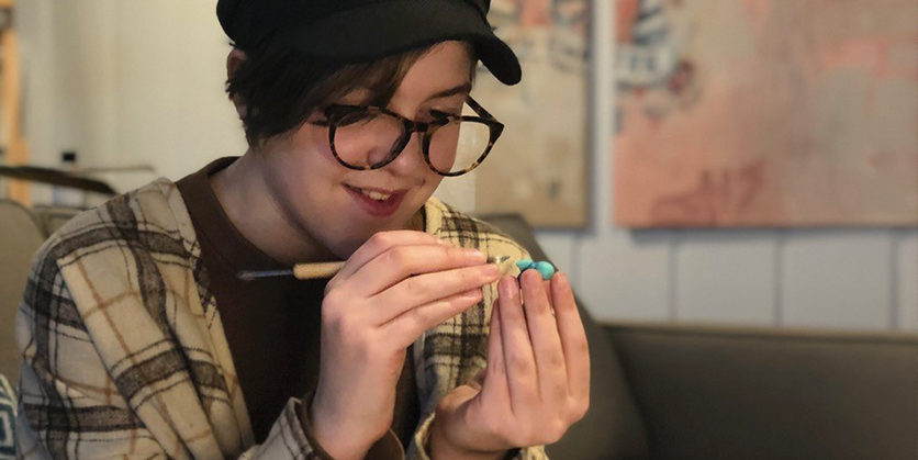 Girl is holding a clay animal and is sculpting it with a tool