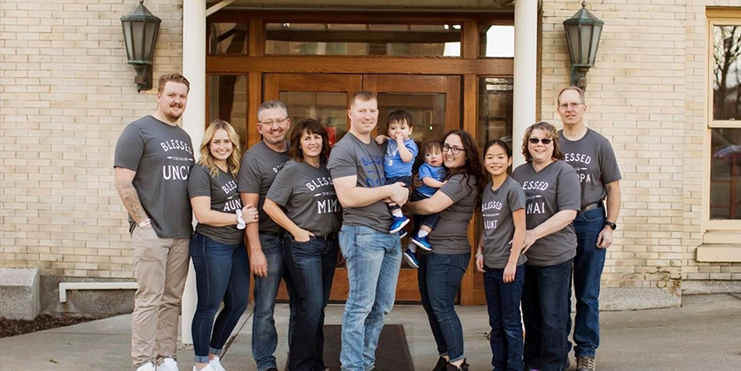 Man and woman holding twin boys, surrounded by an assortment of other people smiling
