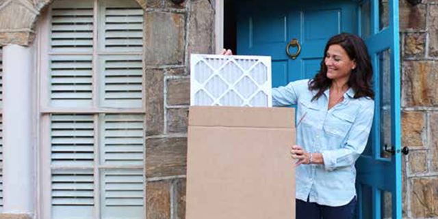 Woman standing at the door, removing a furnace filter from a mailing box