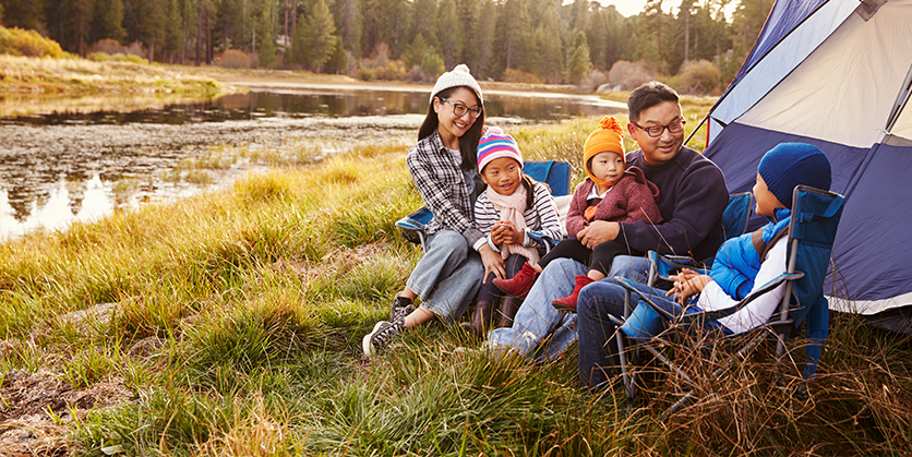 Family sitting outside next to a tent while camping by a river