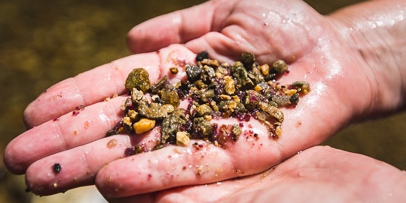 Closeup of person's hand holding sediment containing garnets