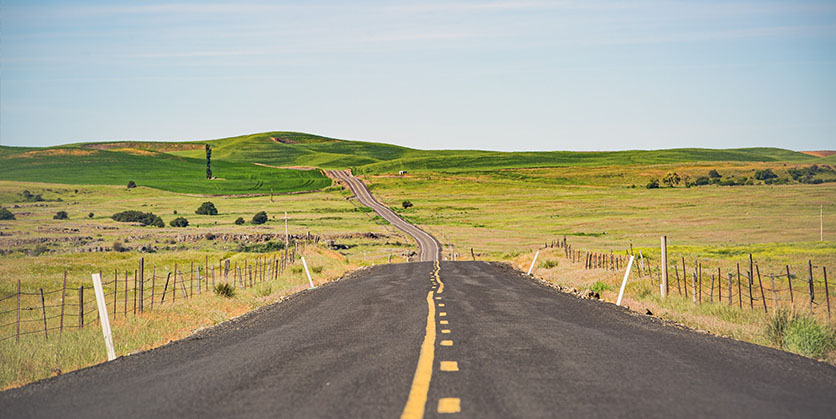 View of road, green fields, and blue sky