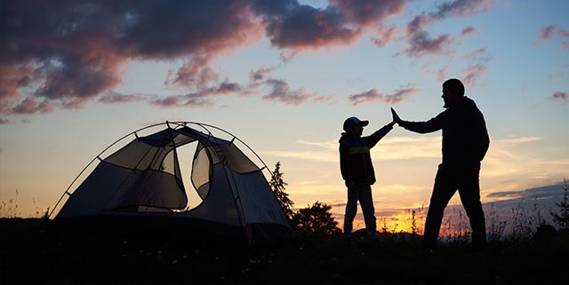 Parent and child high fiving in front of a tent with a campfire