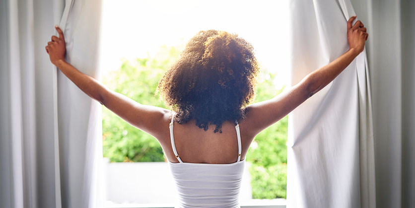 Woman opening curtains with view of sunshine and greenery