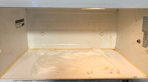 Closeup of the inside of a dirty microwave with a wet paper towels