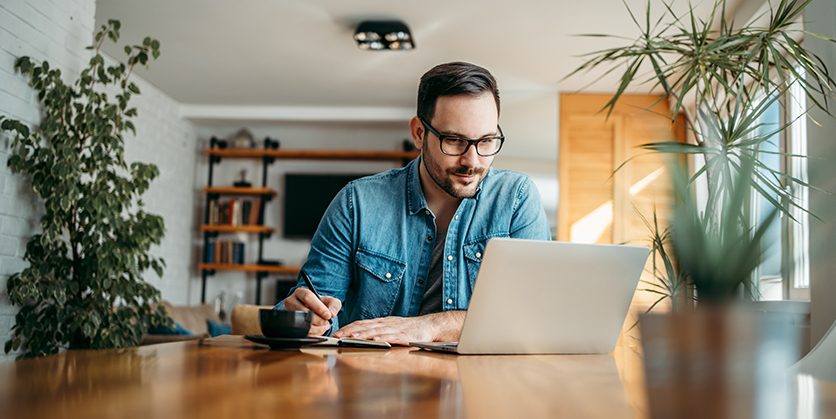 Man taking notes and looking at laptop at home