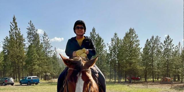 Woman outdoors on horseback, smiling for a photo