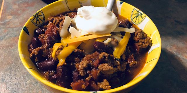 Closeup of a bowl of chili with a blob of sour cream on top with some sprinkled cheese