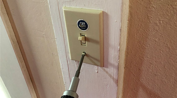 Closeup of a lightswitch and a screwdriver - The screwdriver is unscrewing a screw on the lightswitch