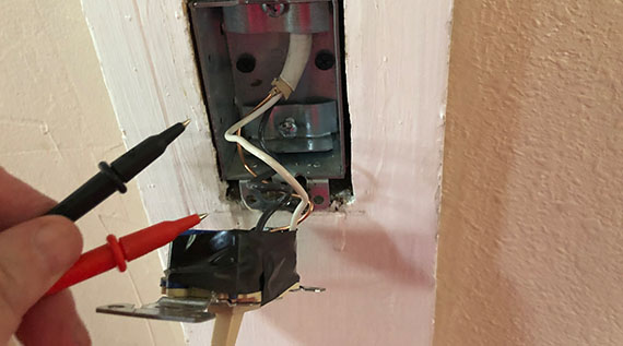 Voltage tester being held up next to the exposed insides of a lightswitch