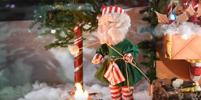 Older man puppet in a festive outfit roasting a marshmallow over a campfire outside