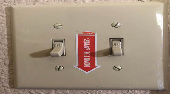 Closeup of a light switch with a sticker on it that says "Down for savings"