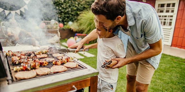 Father and son grilling burgers and kabobs during a barbecue party in their yard