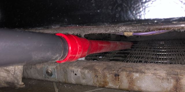 Closeup of the crevice tool on a vacuum cleaning the dust and cat hair underneath a fridge