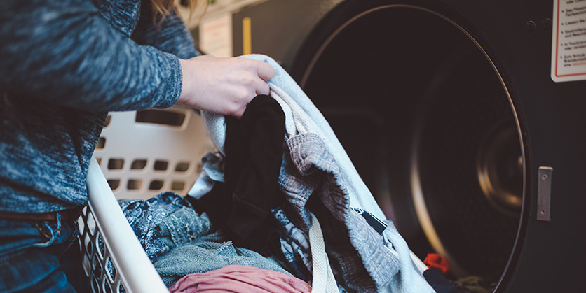 Closeup of woman holding a laundry basket, putting clothes into a clotheswasher