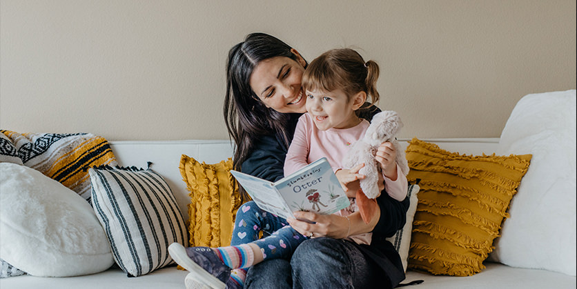 Mother reads book to a little girl, who is sitting on her lap