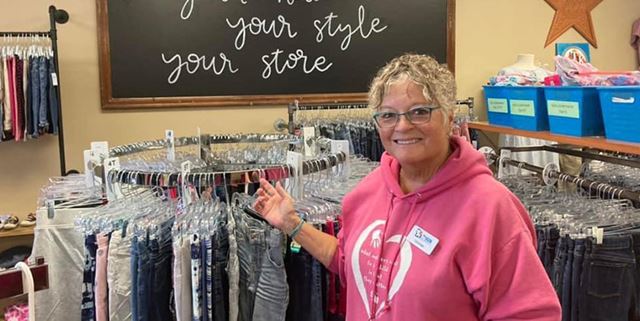 Volunteer woman stands in front of a rack of clothes at Teen and Kid Closet