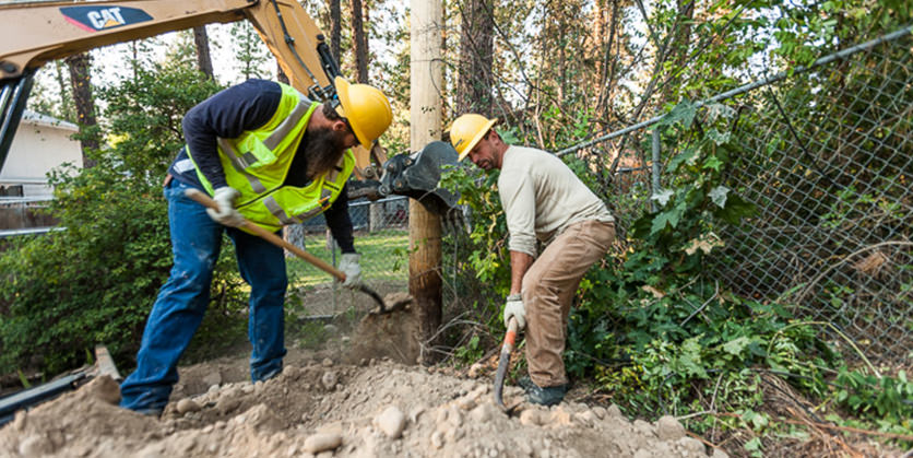 Two Avista workers in hard hats and yellow vests digging with shovels