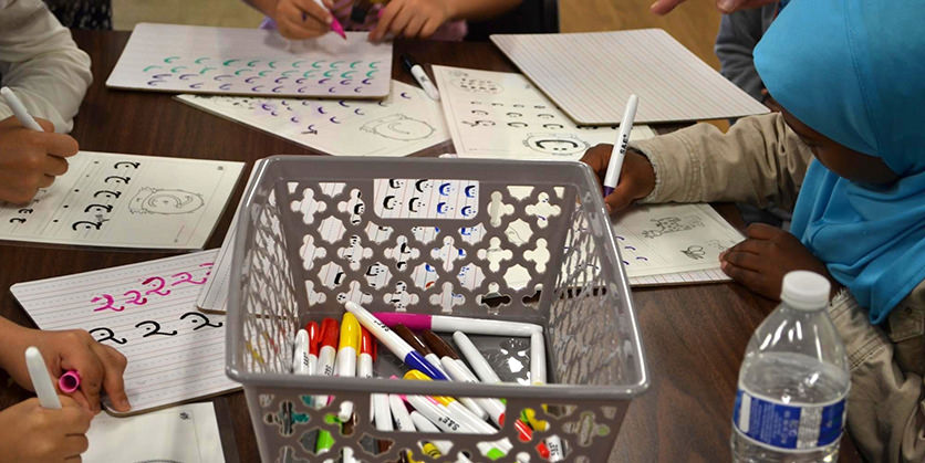 Children practicing Arabic on paper worksheets