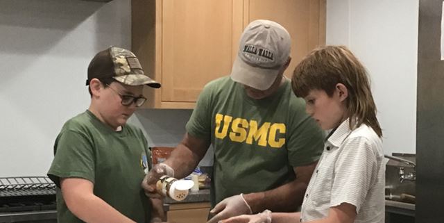 Man helping two teen boys learn how to cook in a kitchen