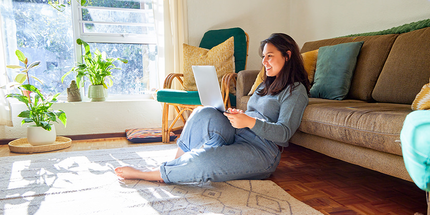 Woman sitting on floor in her living room, looking at laptop