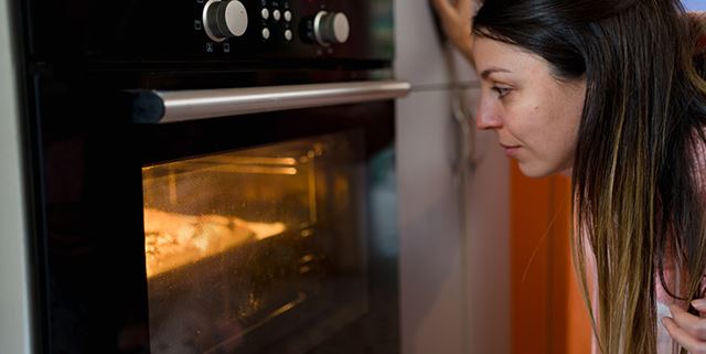 Woman checking food in the oven by looking through the oven's glass window