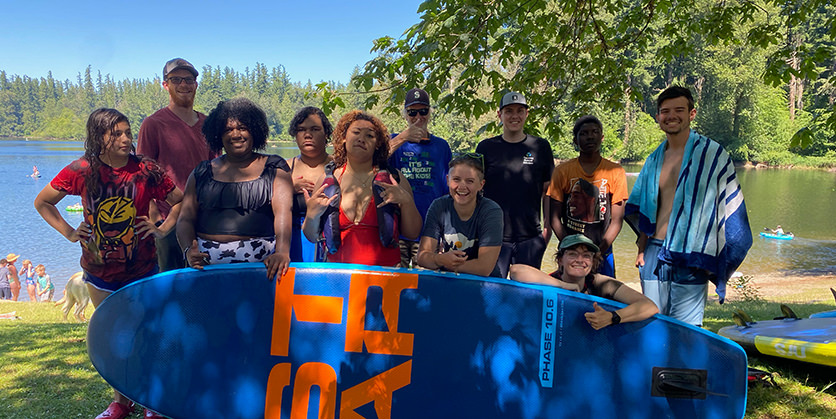 Group of young people posing by a surfboard by the lake