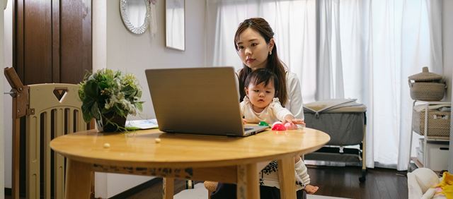 Mother on laptop while holding baby at home