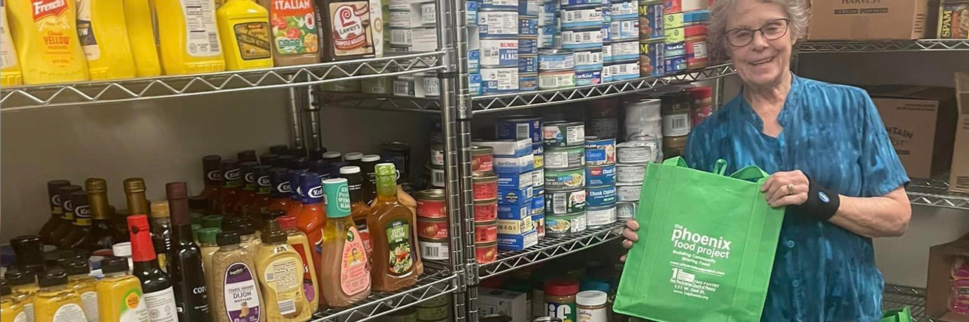 Woman holds a green cloth bag while standing next to racks of non-perishable food at a food pantry.