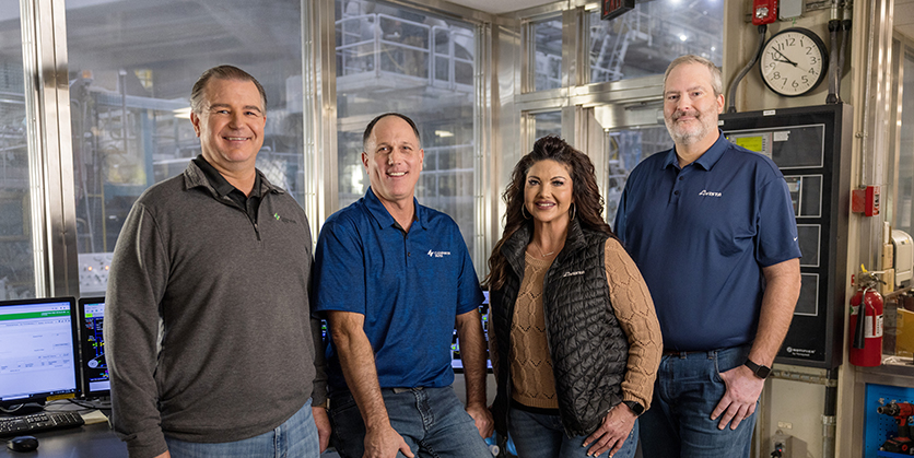 Four people are standing in a row and smiling