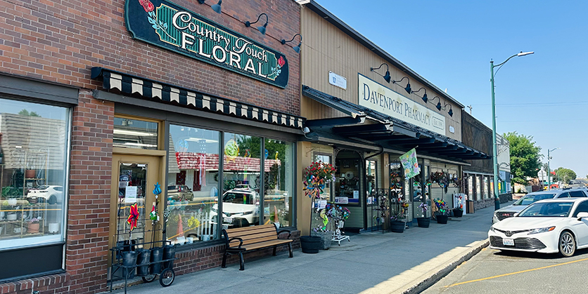 Two buildings from the outside, one is a brick building with a sign that says Country Touch Floral and the other is a wood building with a sign that says Davenport Pharmacy.