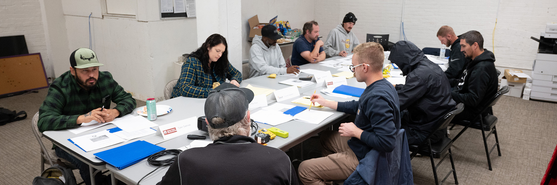 Ten people sit at a rectangular table together, their are many papers in front of them and name tags.
