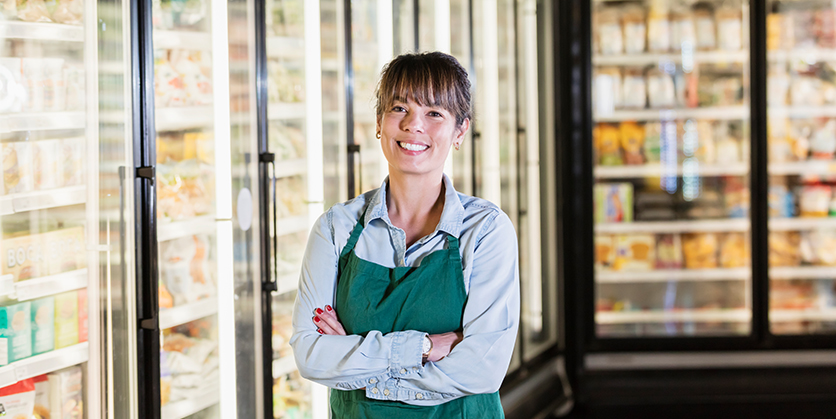 Grocer employee wearing an apron, standing in the refrigerated section at the grocery store