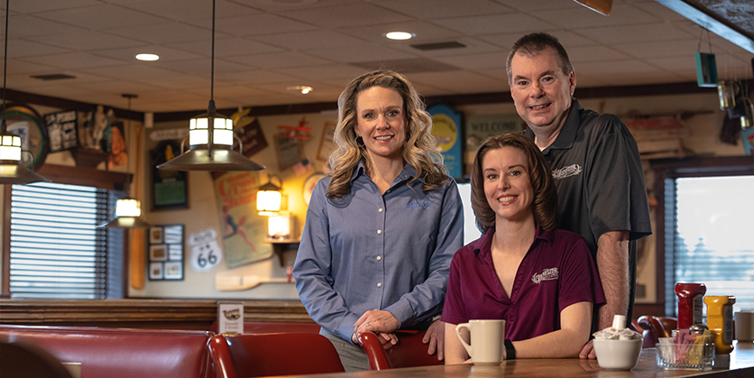 Three people sit in the Harvester Restaurant, smiling