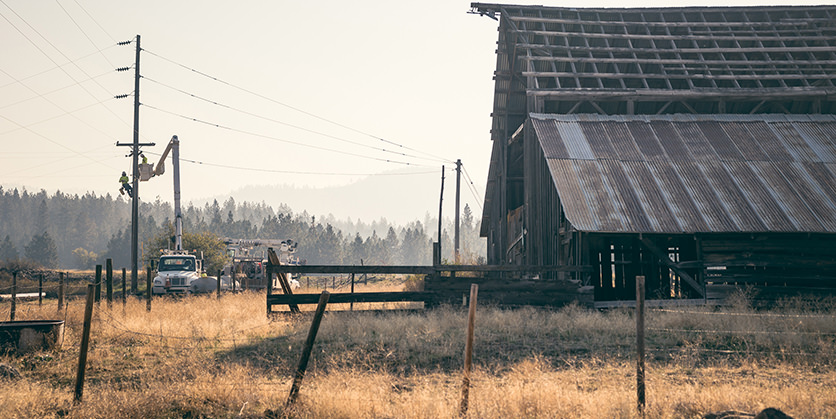 Linemen working on a power pole in front of an old barn