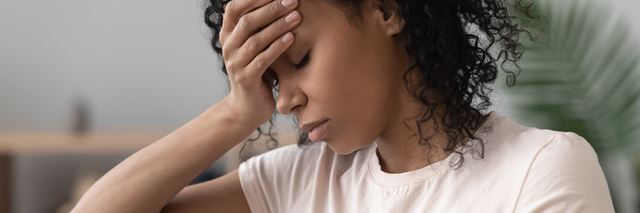 Woman has her hand pressed against her forehead with her eyes closed, she looks uncomfortable as if she's suffering from a headache.
