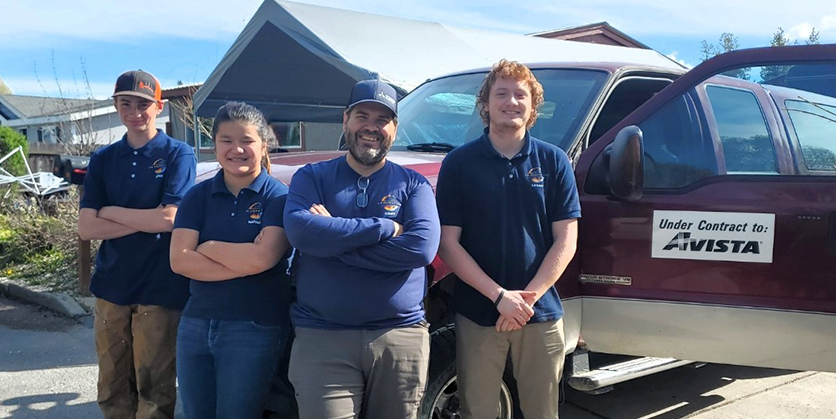 Four workers stand outside by a truck, which is under contract to Avista