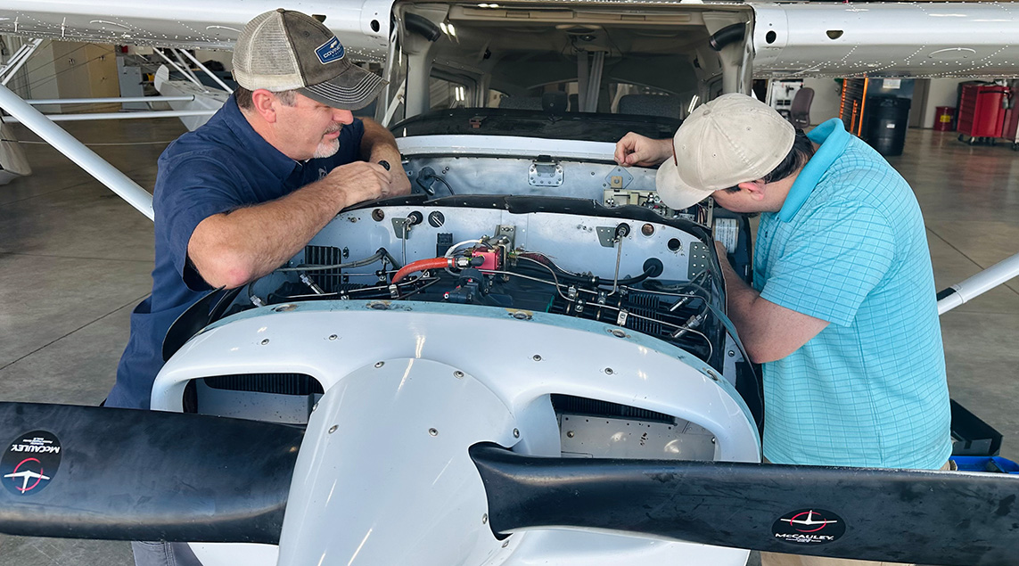 Two men work on a propeller plane's engine.