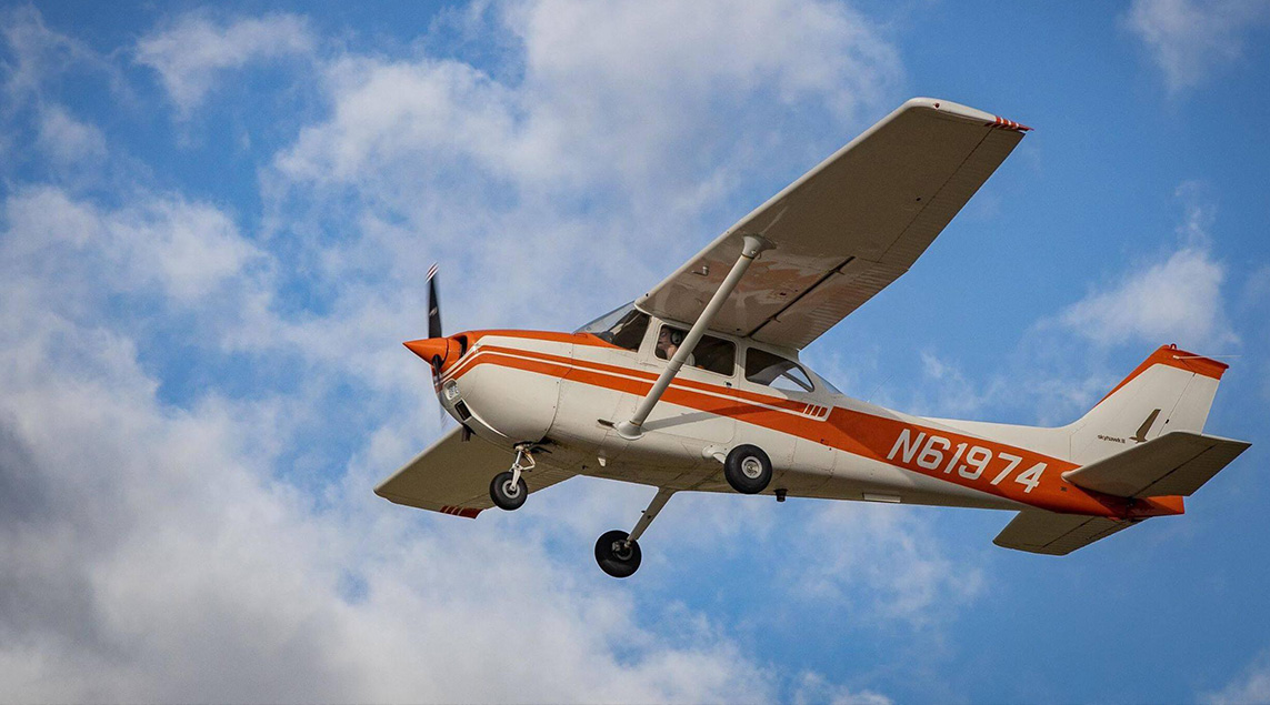 A white and orange propeller airplane is flying on a blue sky, cloudy day.